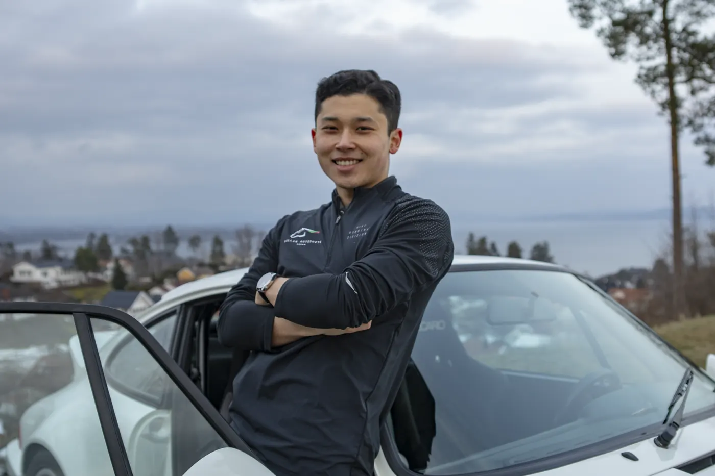 Imran Bakijev smiler foran en hvit Porsche med fjorden i bakgrunnen